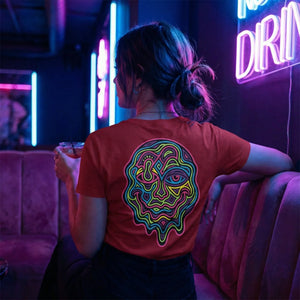 Woman wearing red t-shirt with colorful psychedelic face design back, sitting in neon-lit bar holding drink