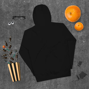Black unisex premium pullover hoodie on dark textured surface with orange pumpkins, glasses, and Halloween candy