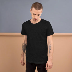 Man with tattoos wearing black heather unisex staple t-shirt against gray and beige background