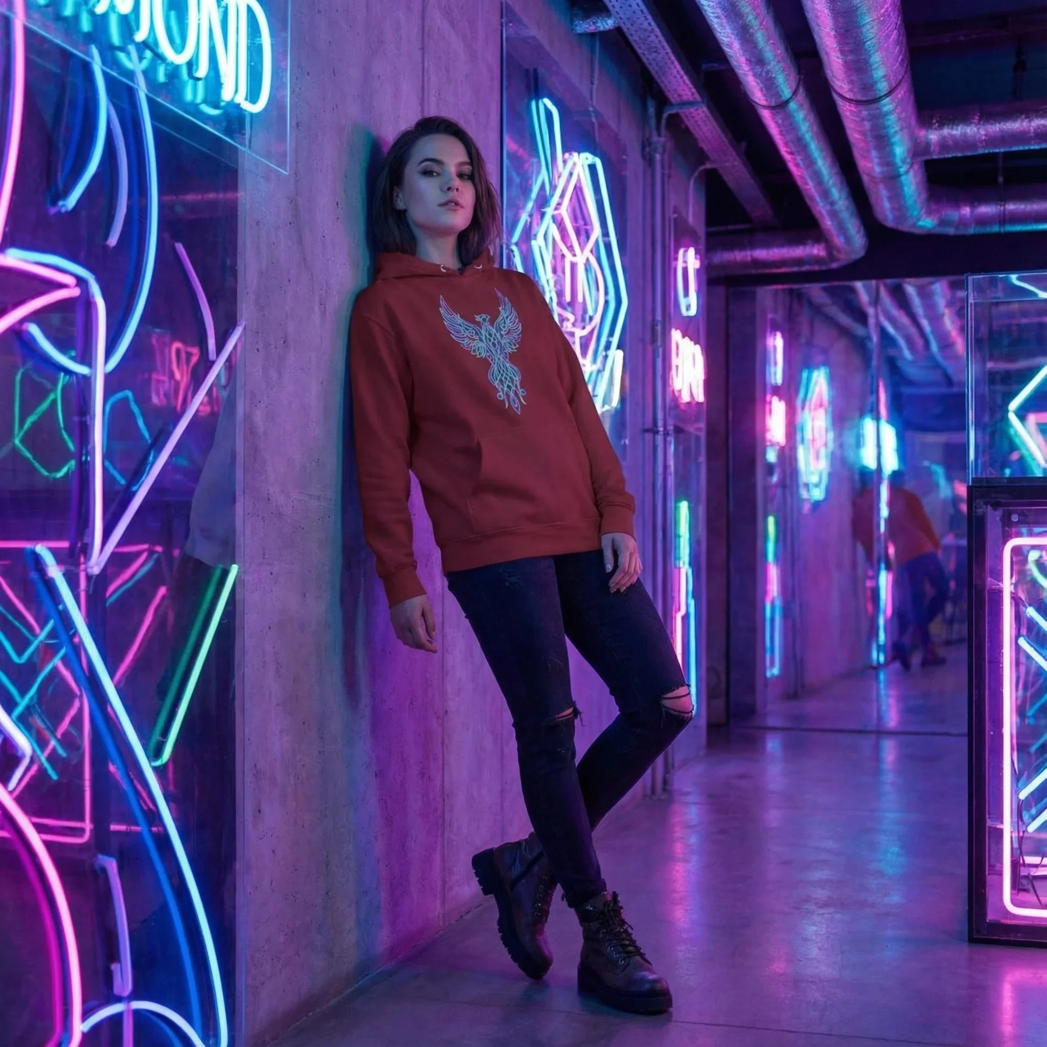 Woman wearing red hoodie with phoenix design posing in neon-lit urban corridor with reflective walls