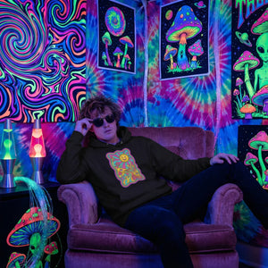 Young man wearing a psychedelic black hoodie with sun and mushroom art, sitting in a vibrant tie-dye room with neon mushroom posters and lava lamps