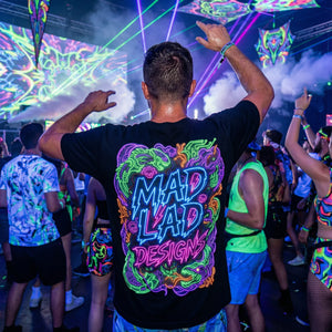 Man wearing psychedelic Mad Lad Designs neon graphic T-shirt at vibrant electronic music festival with colorful laser lights