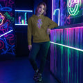 Young woman in neon-lit urban setting wearing olive hoodie with psychedelic flame design and dark jeans