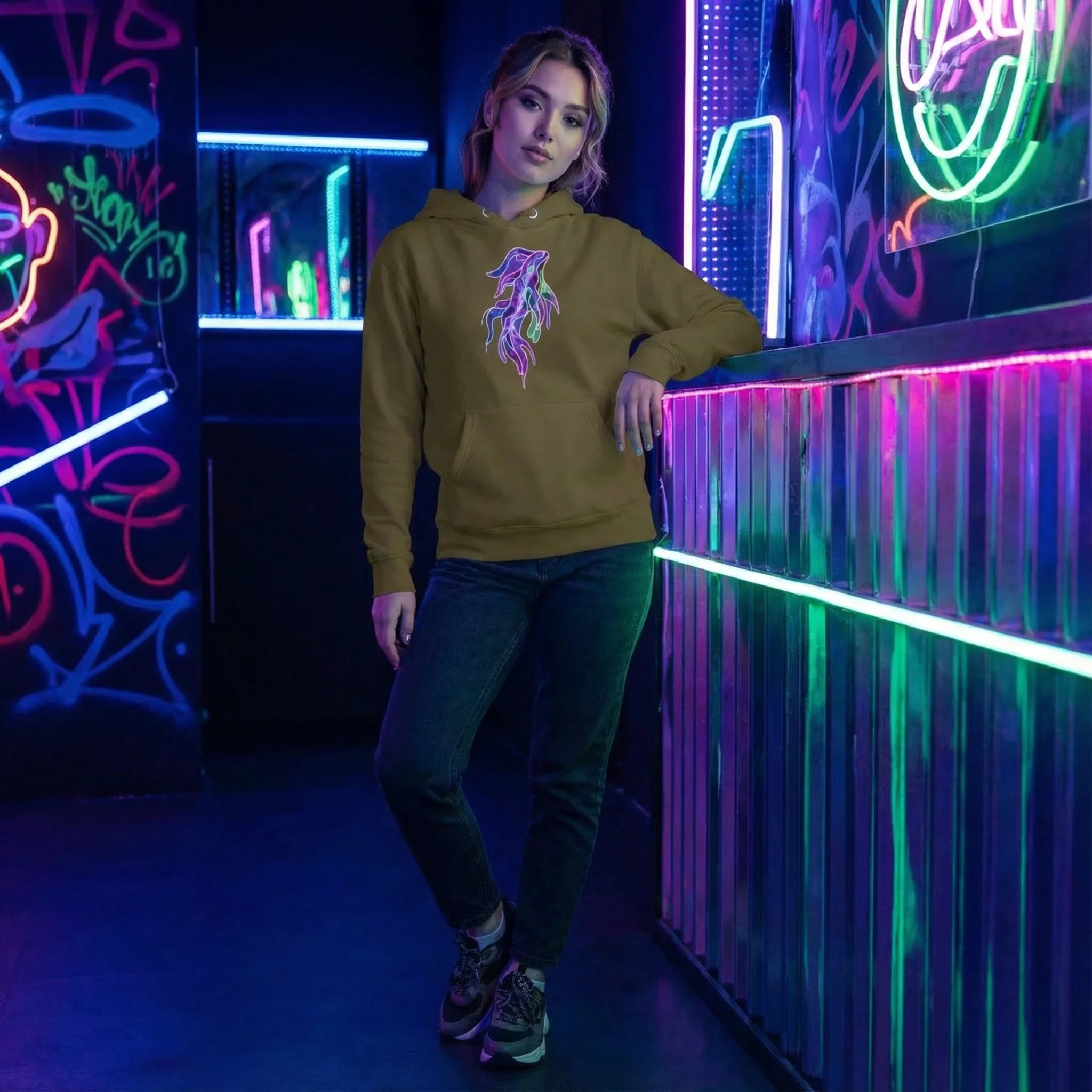 Young woman in neon-lit urban setting wearing olive hoodie with psychedelic flame design and dark jeans