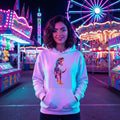 Young woman in white hoodie with dinosaur print at colorful neon-lit amusement park at night