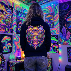 Person wearing black hoodie with colorful psychedelic eye and mushroom design, surrounded by neon art posters and crystals
