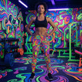Woman wearing psychedelic neon leggings and black sports bra in vibrant, colorful gym with neon swirl and mushroom patterns