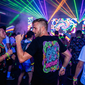 Man dancing at neon light party wearing black Mad Lad Designs T-shirt with bright psychedelic logo
