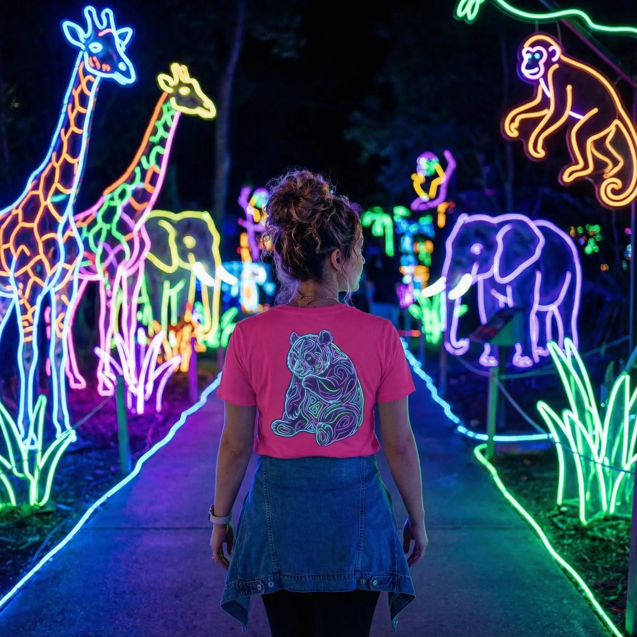 Woman wearing pink tiger t-shirt walking through neon animal light display with giraffes, elephants, and monkey