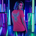 Woman with blue hair wearing a pink t-shirt featuring a neon phoenix design in a vibrant neon-lit room