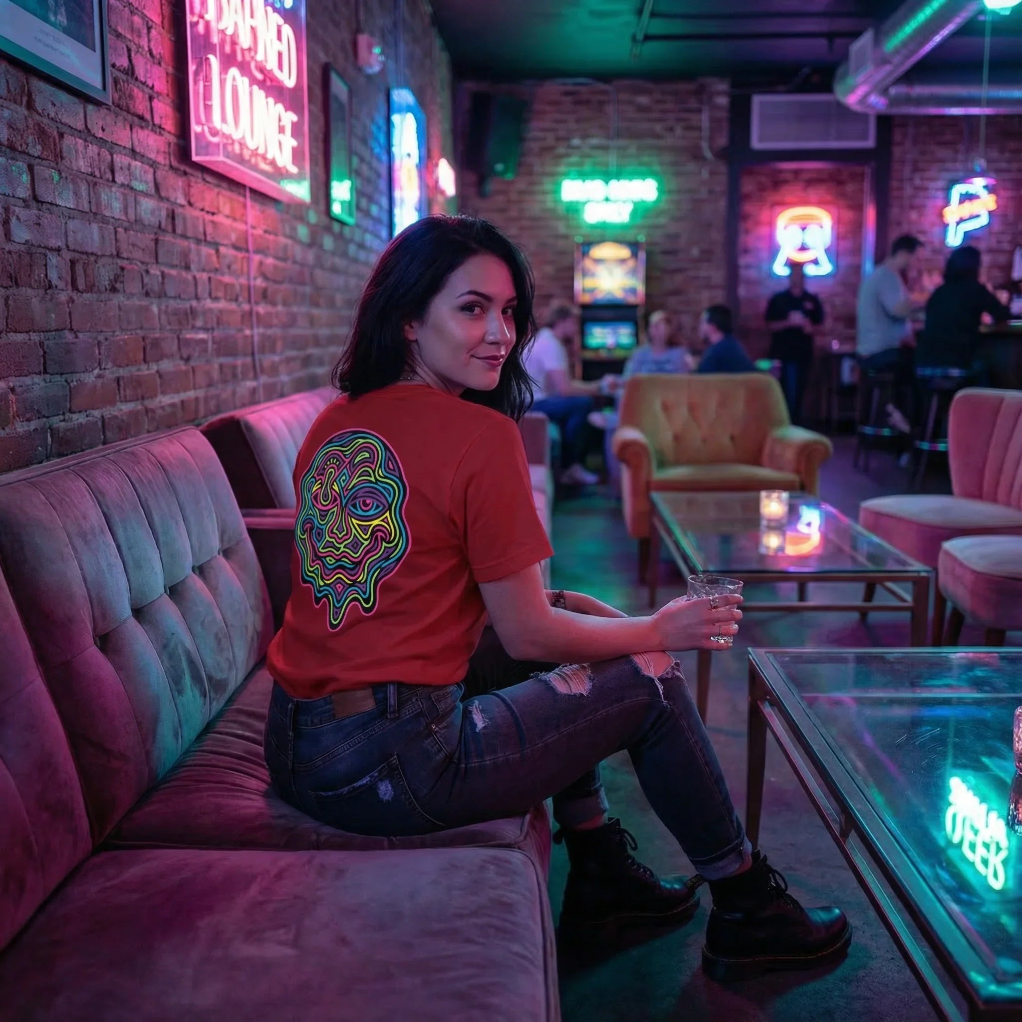 Woman wearing red psychedelic graphic T-shirt and ripped jeans sitting on velvet sofa in neon-lit lounge bar