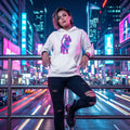 Young woman in ripped jeans and white hoodie with colorful cat graphic posing on city street at night with neon lights