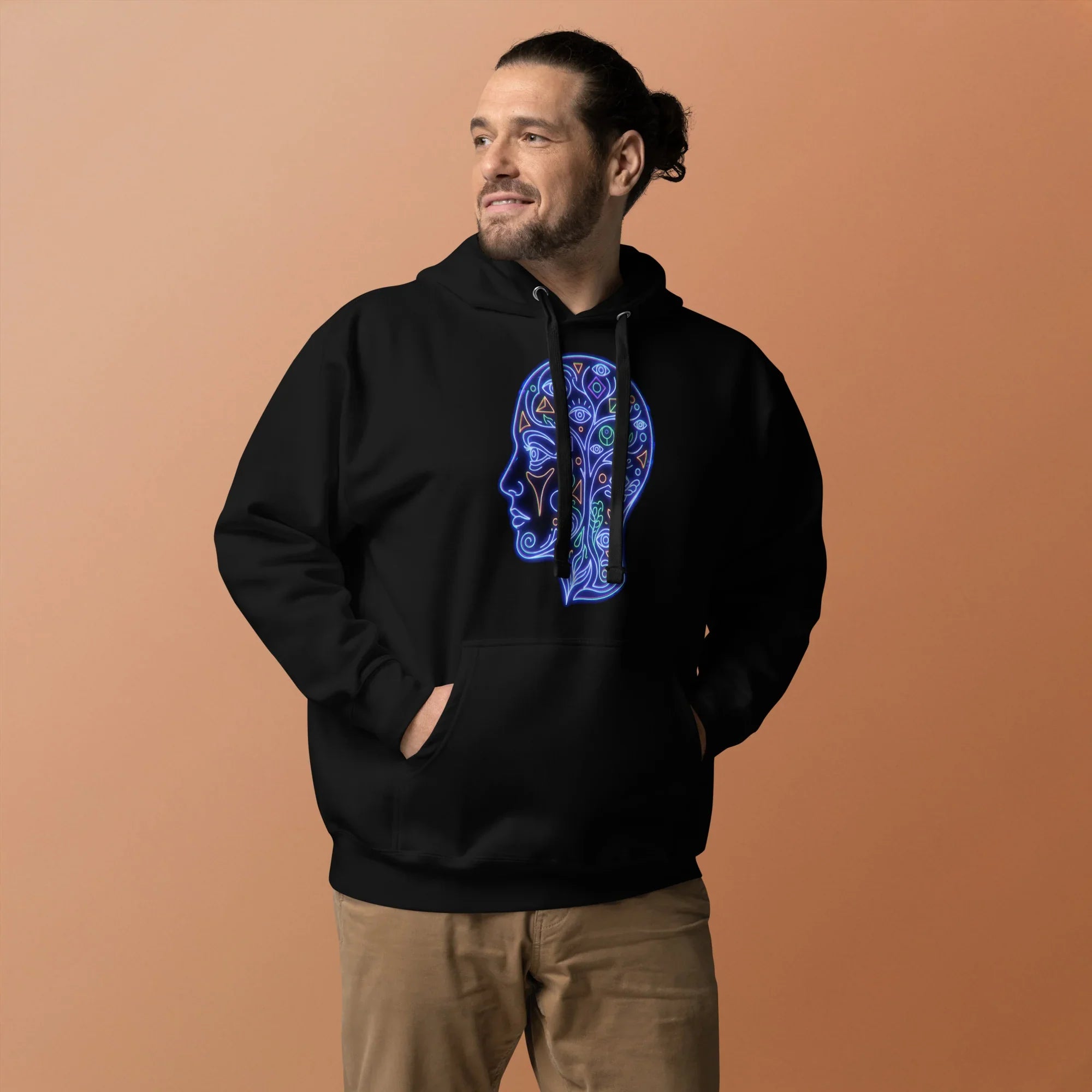 Man wearing black unisex premium hoodie with neon blue psychedelic head design, standing against brown background