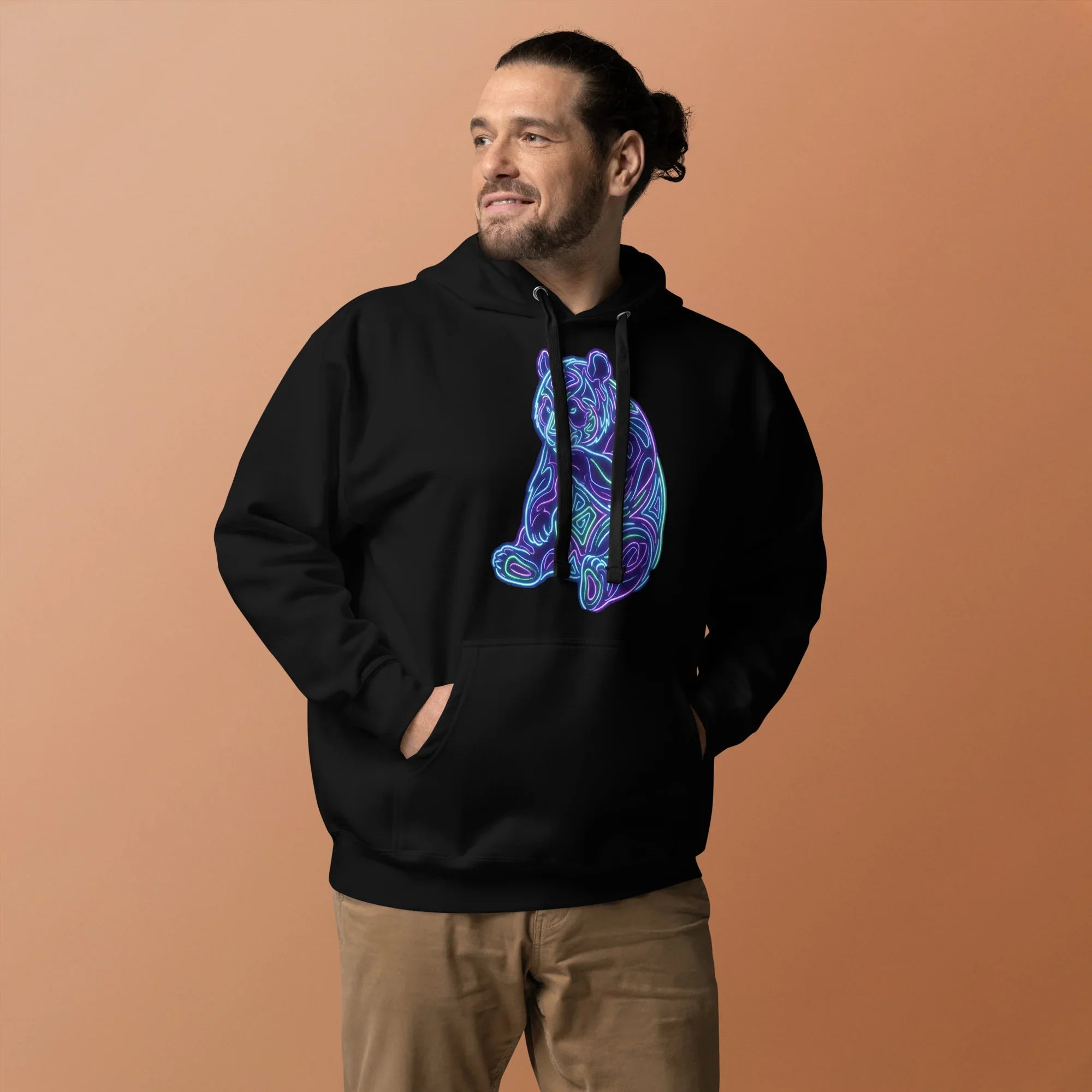 Man wearing black premium pullover hoodie with neon psychedelic bear graphic, beige pants, neutral background
