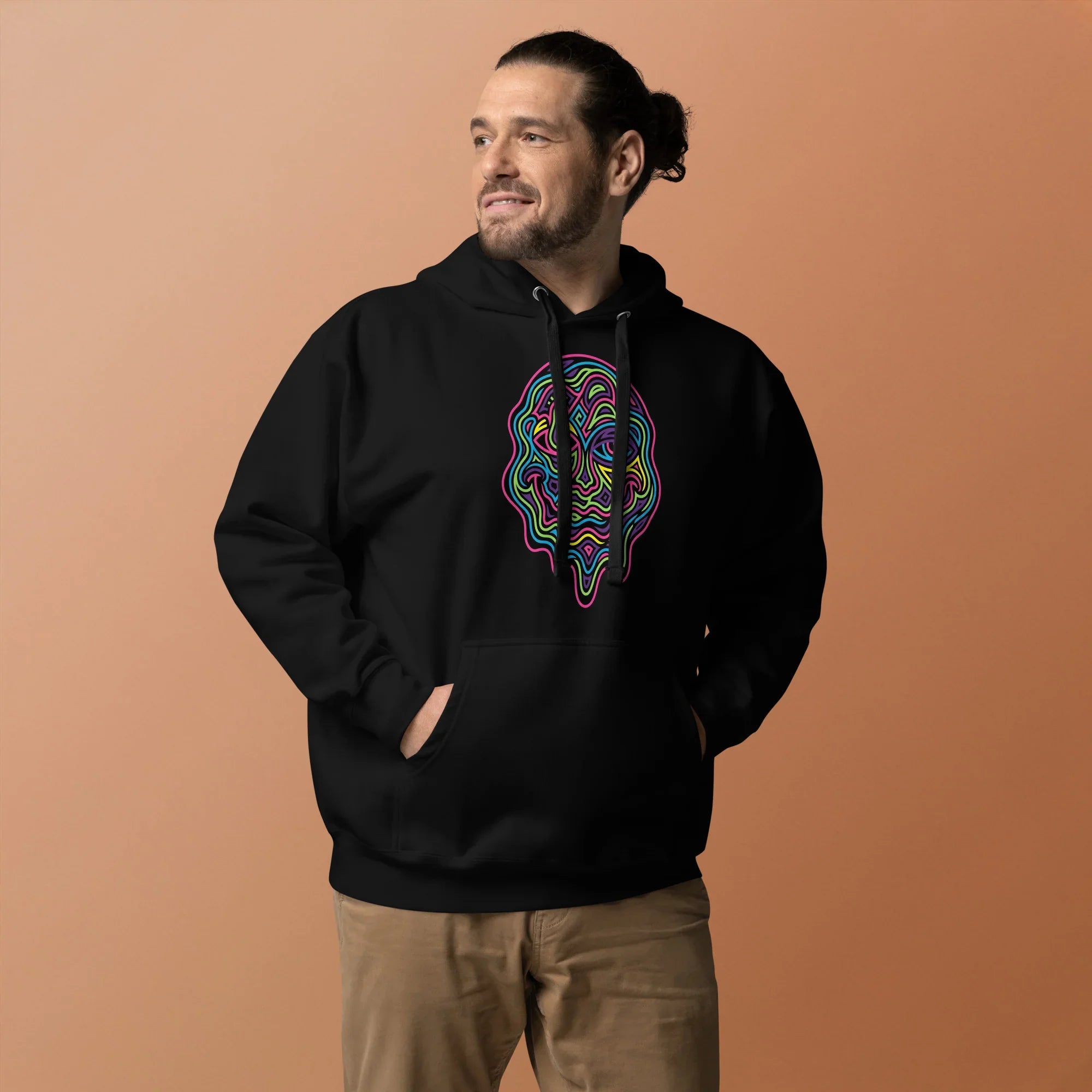 Man wearing black unisex pullover hoodie with colorful psychedelic abstract face design, beige pants, neutral background