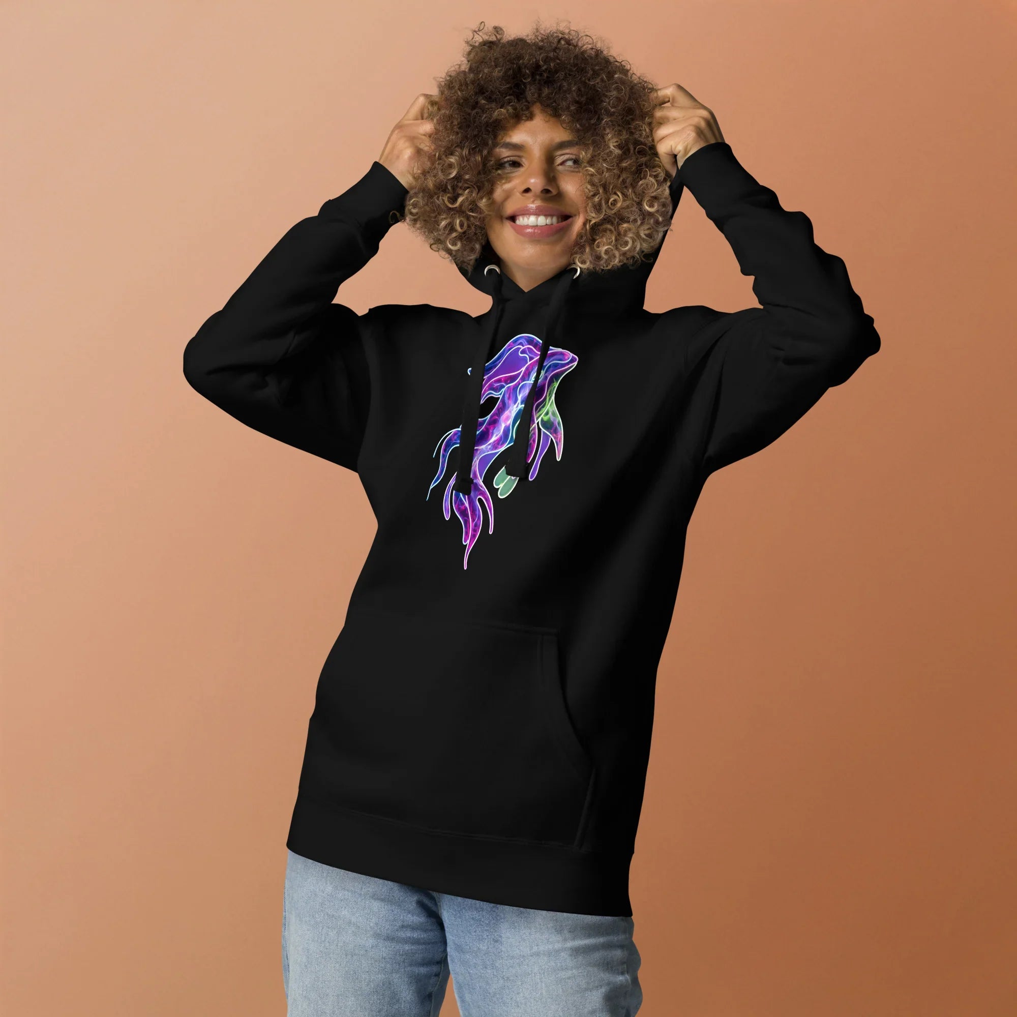 Smiling person wearing black unisex premium hoodie with vibrant neon psychedelic jellyfish design on peach background