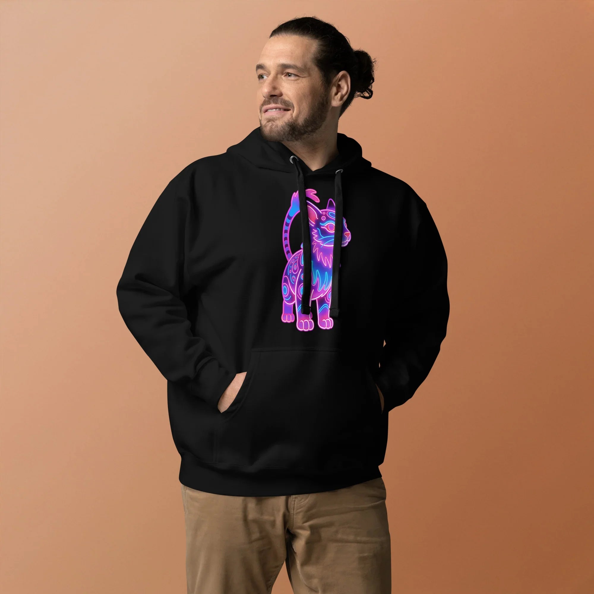 man wearing black unisex hoodie with neon pink and blue cat graphic on front against peach background