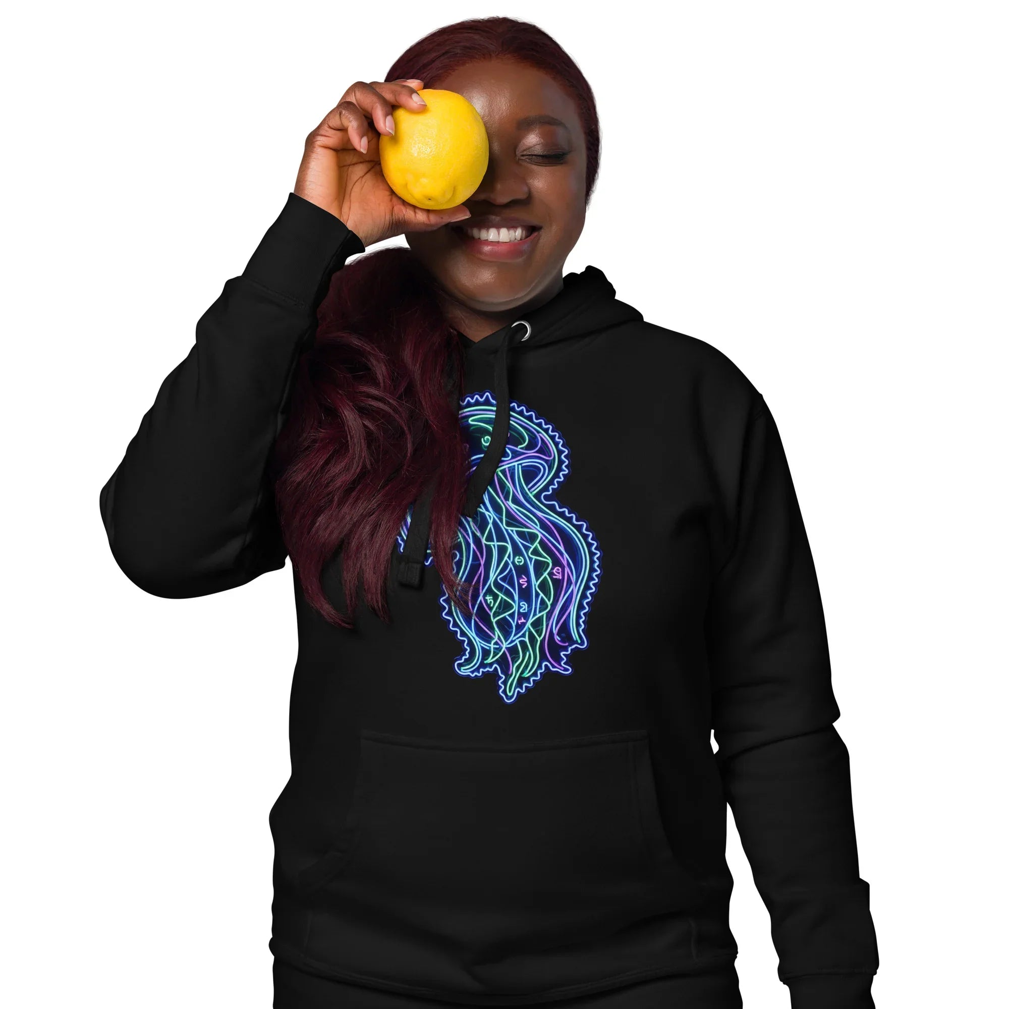 Smiling woman wearing black hoodie with colorful psychedelic jellyfish design holding lemon over eye