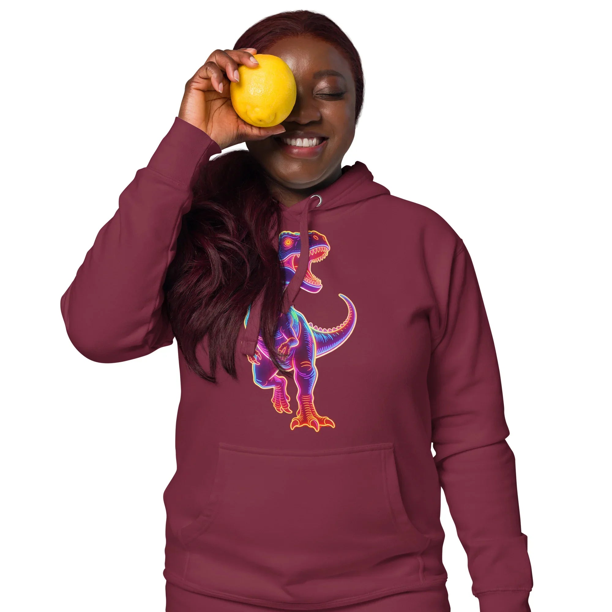 Smiling woman wearing maroon hoodie with colorful neon T-Rex design holding a lemon over one eye