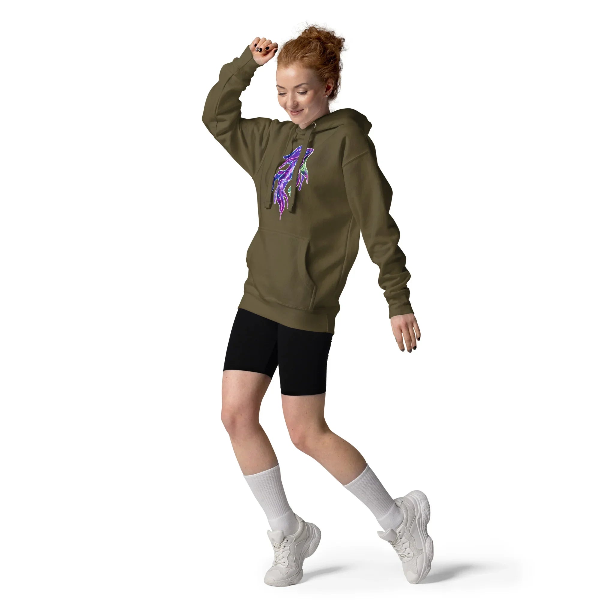Red-haired woman dancing in military green unisex premium pullover hoodie with neon feather design, black shorts, white socks, and sneakers