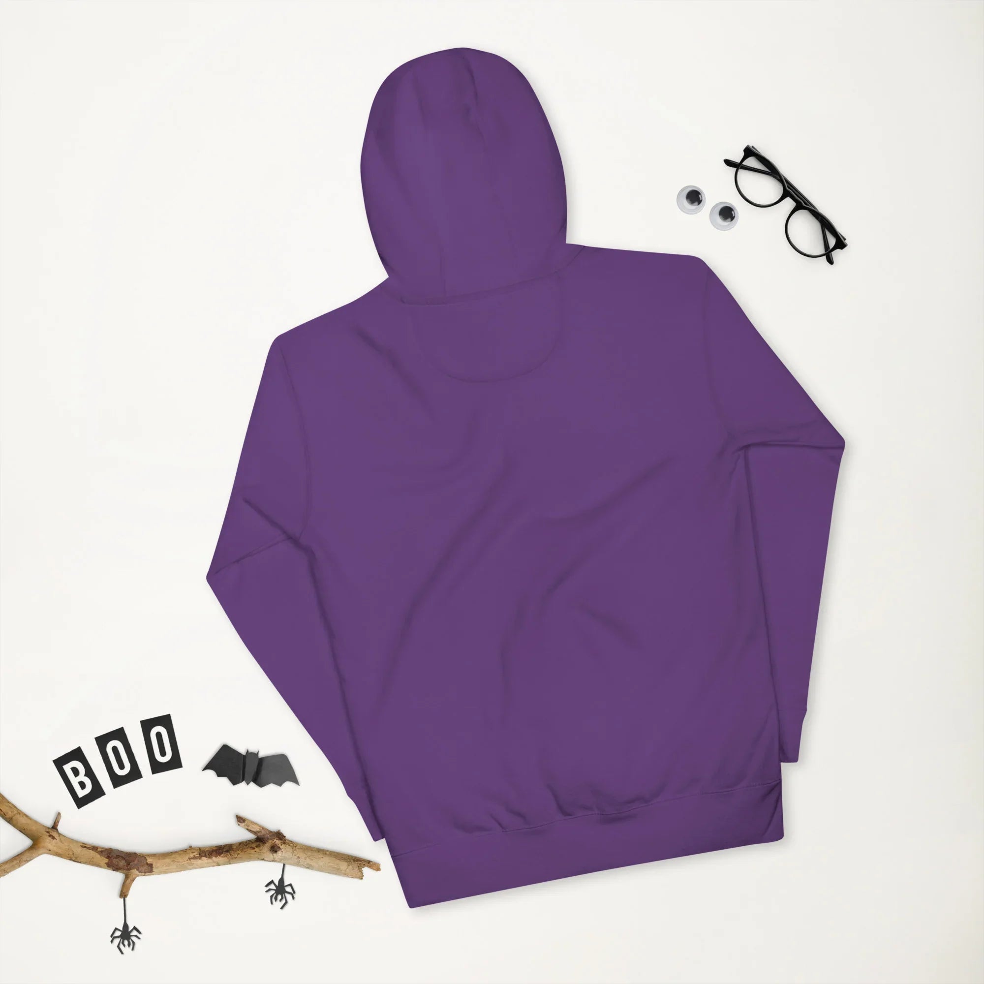 Purple unisex premium pullover hoodie flat lay with black glasses, googly eyes, and Halloween decor including bats and spiders