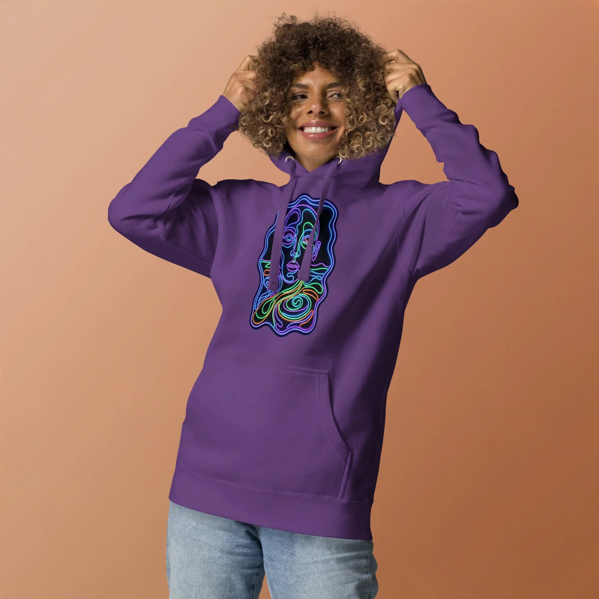 Smiling woman wearing purple unisex hoodie with colorful psychedelic face line art on front against tan background