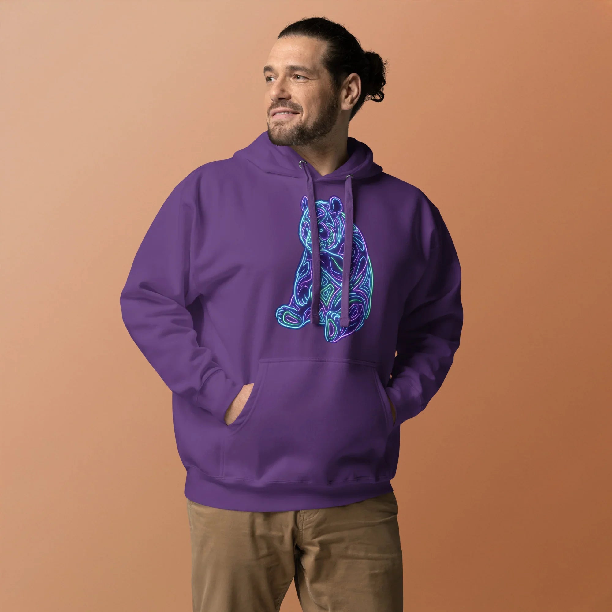 Man wearing purple pullover hoodie with neon psychedelic bear graphic and tan pants on beige background
