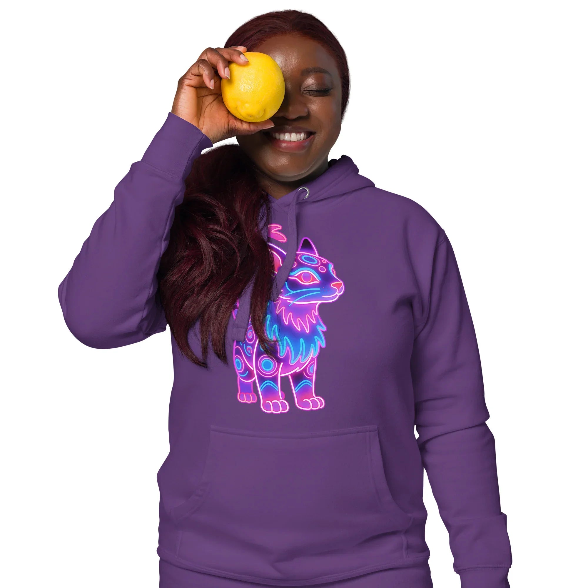 Smiling woman in purple hoodie with neon cat graphic holding lemon over one eye