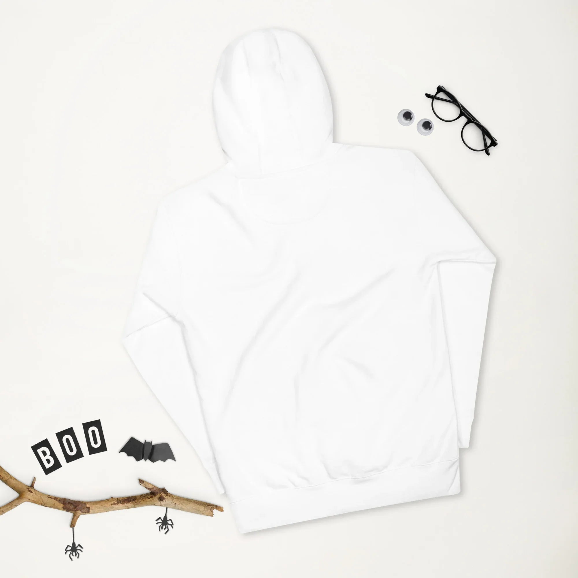 White unisex premium pullover hoodie laid flat with Halloween decorations including a twig, paper bats, spiders, 'BOO' letters, and glasses with googly eyes
