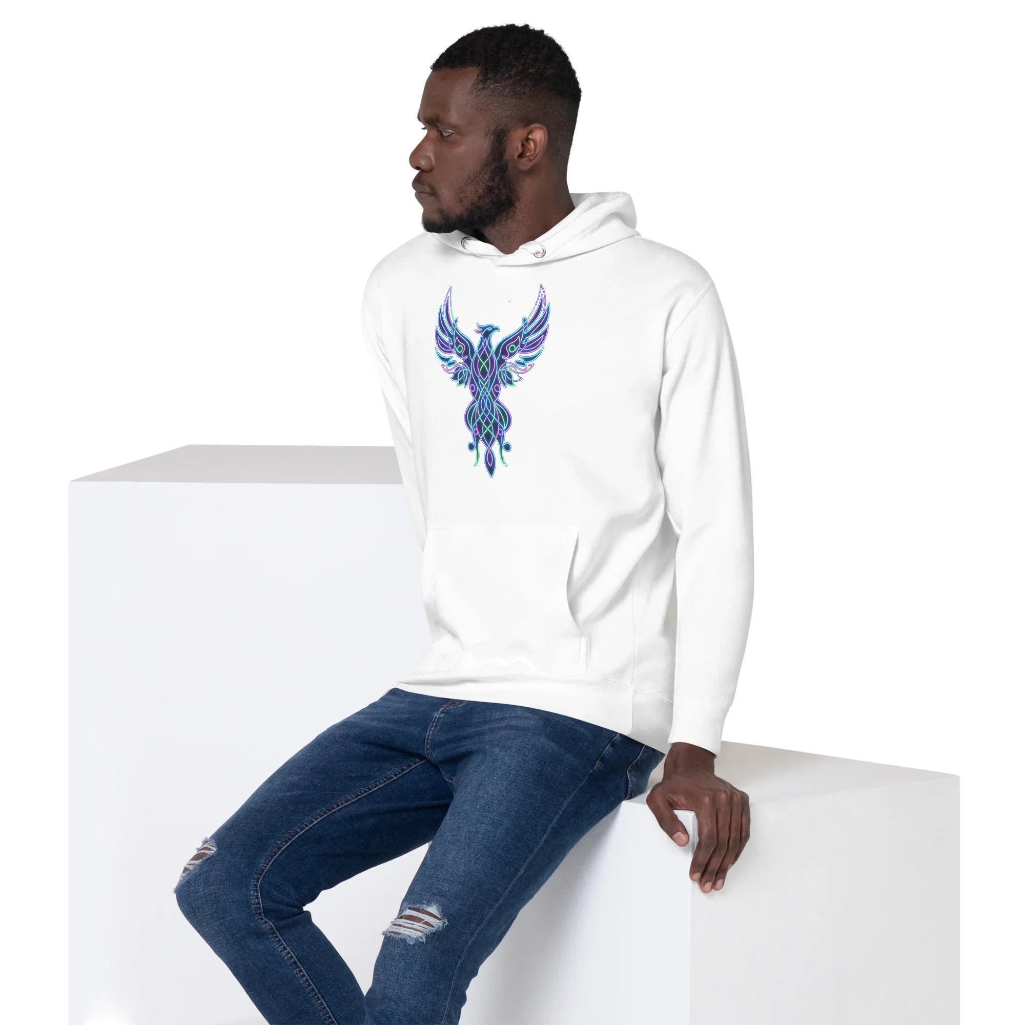 Man wearing white unisex premium pullover hoodie with blue and purple psychedelic phoenix design sitting on white cube
