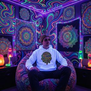 Man wearing white hoodie with psychedelic face print sitting on colorful bean bag in neon lit room with psychedelic mandala tapestries and lava lamps
