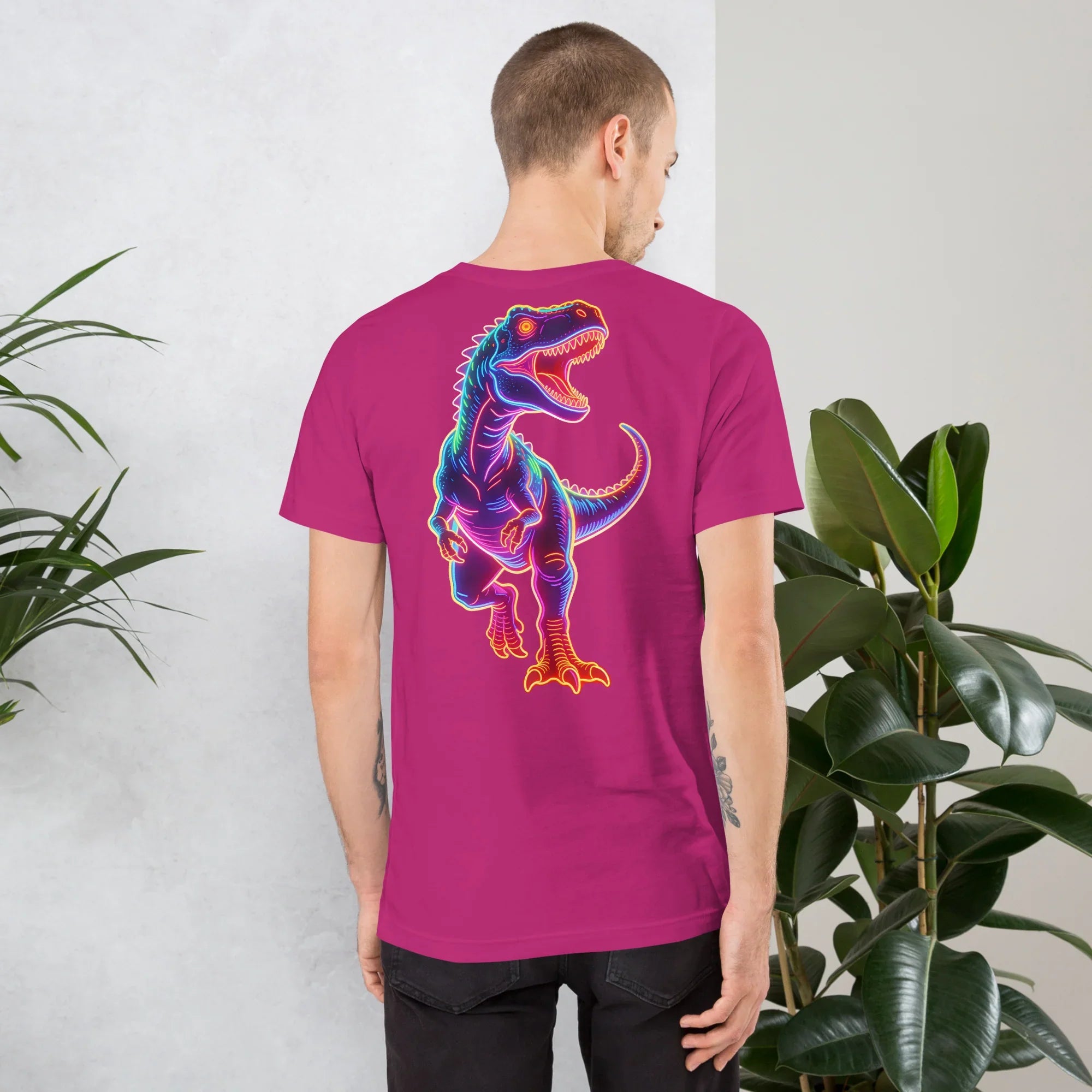 Man wearing berry unisex t-shirt with neon colorful dinosaur graphic on back, standing indoors