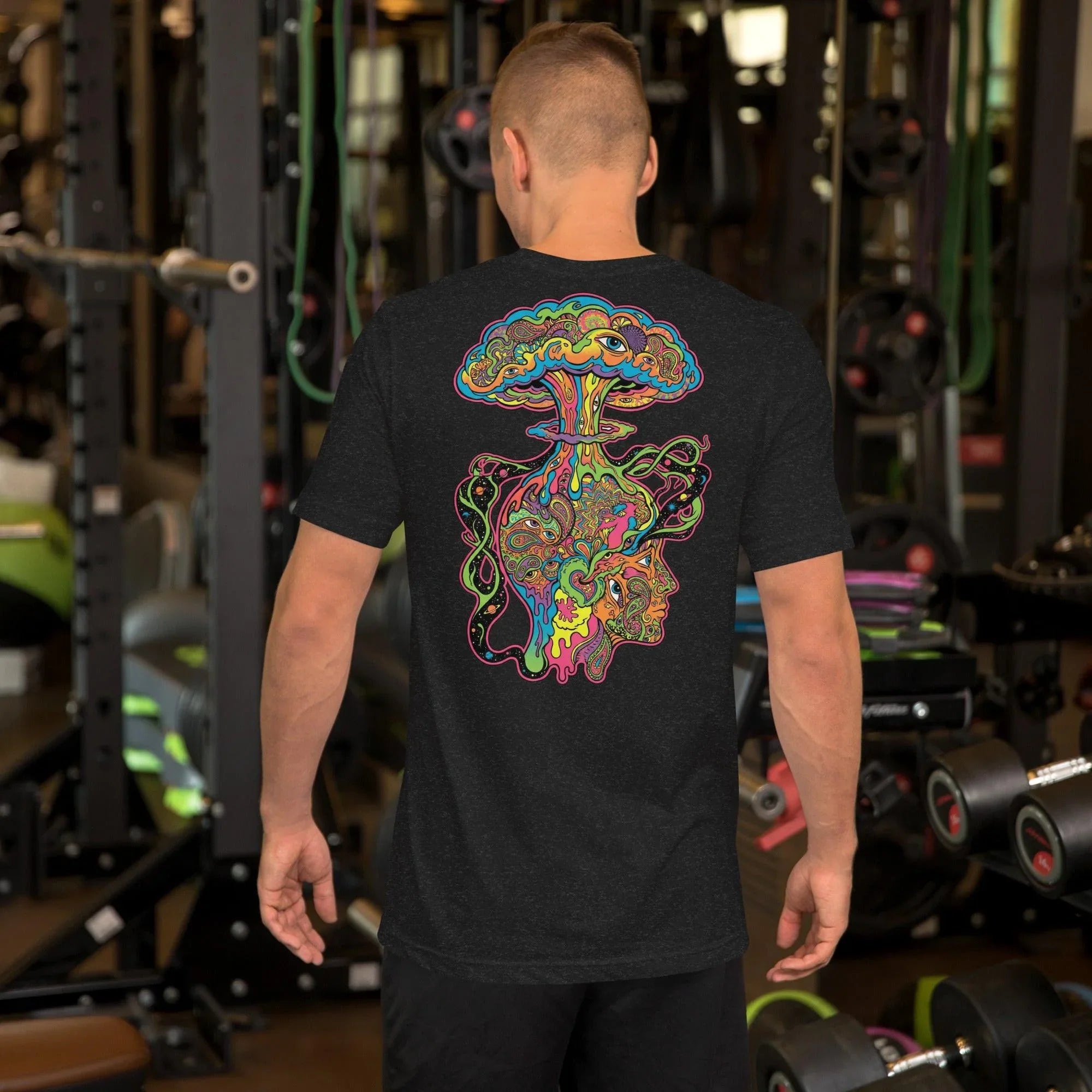 Man in gym wearing black heather unisex t-shirt with colorful psychedelic art showing an exploding mushroom cloud and intricate face design