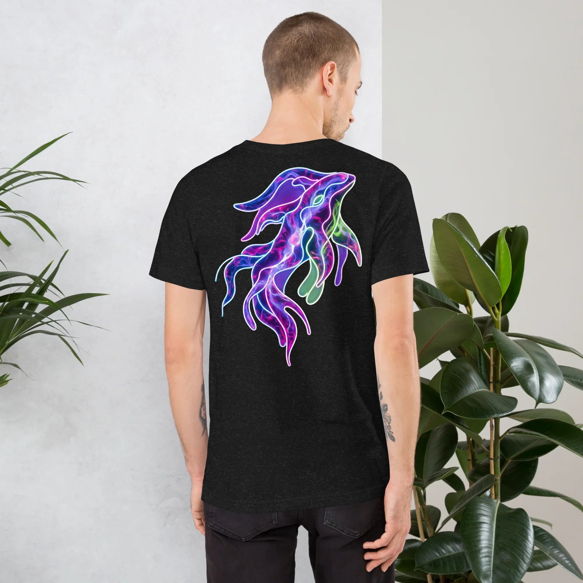 Back of black heather unisex staple t-shirt with colorful neon squid art design worn by male model indoors with green plants