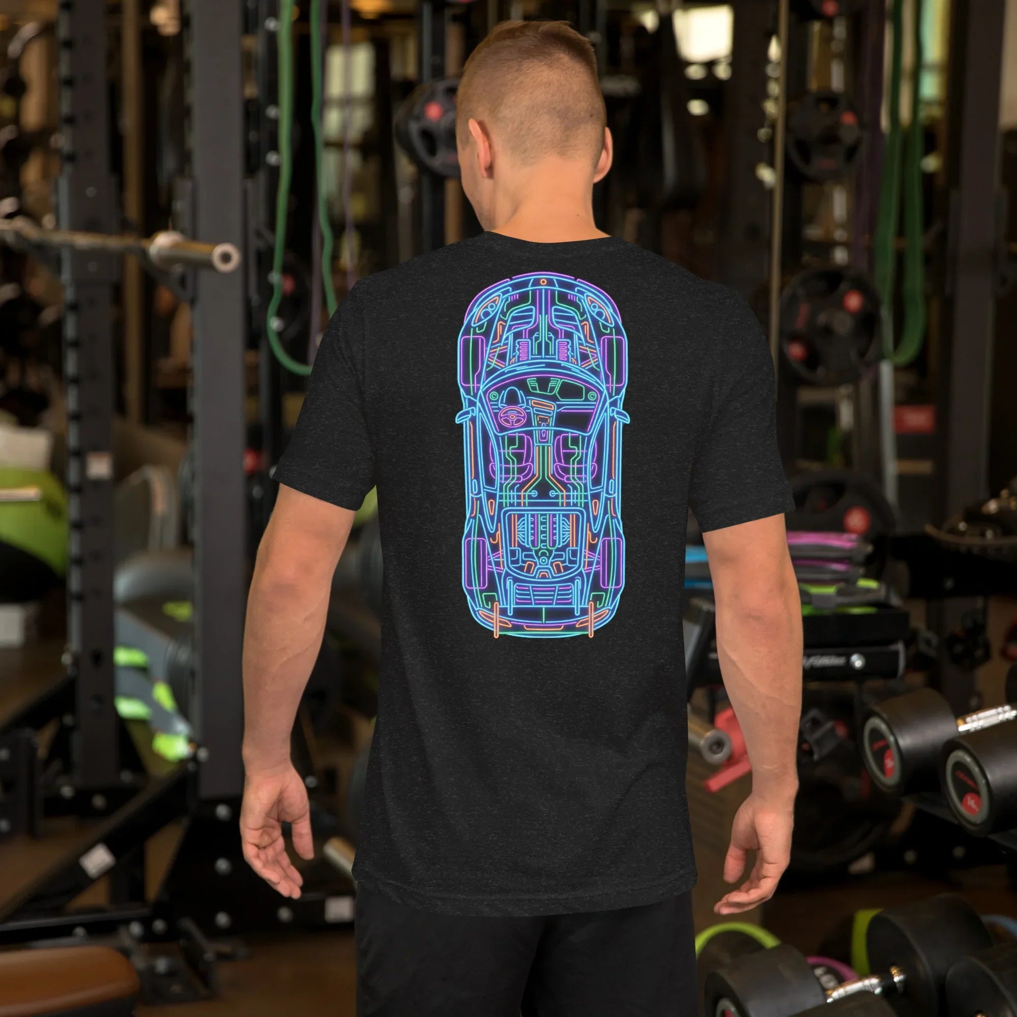 Man wearing black heather t-shirt with neon car blueprint design standing in gym with weights and equipment