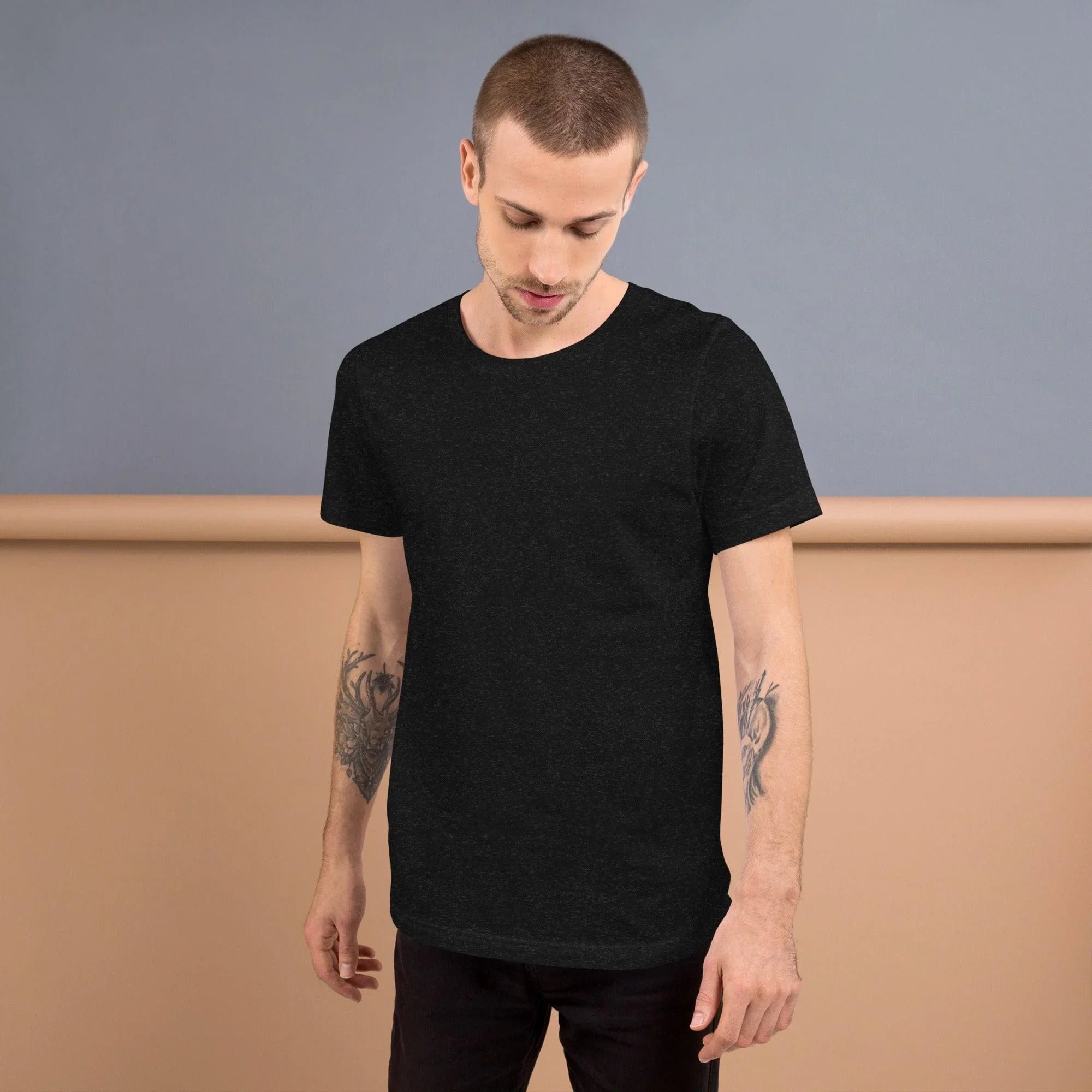 Man with tattoos wearing black heather unisex staple t-shirt against gray and beige background