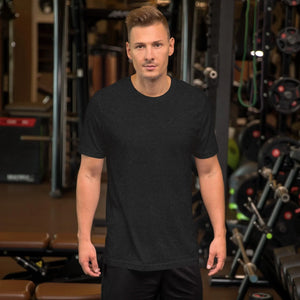 Man in black heather unisex staple t-shirt standing in gym with weights and equipment background