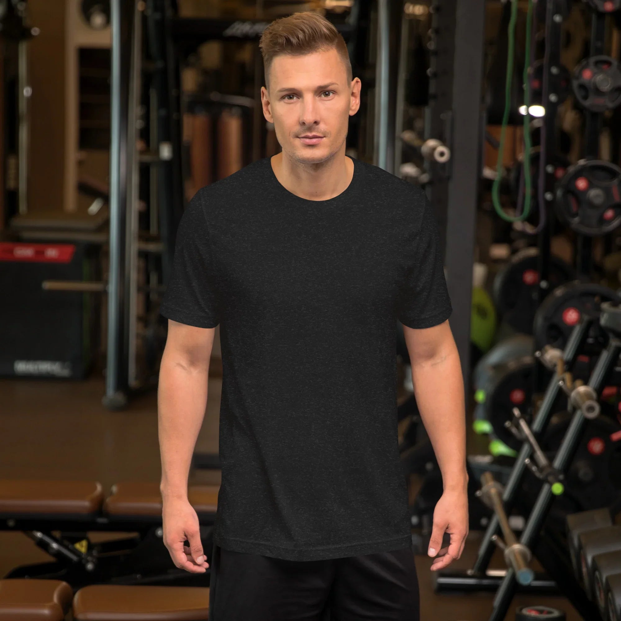 Man wearing plain black heather unisex staple t-shirt in gym with weightlifting equipment