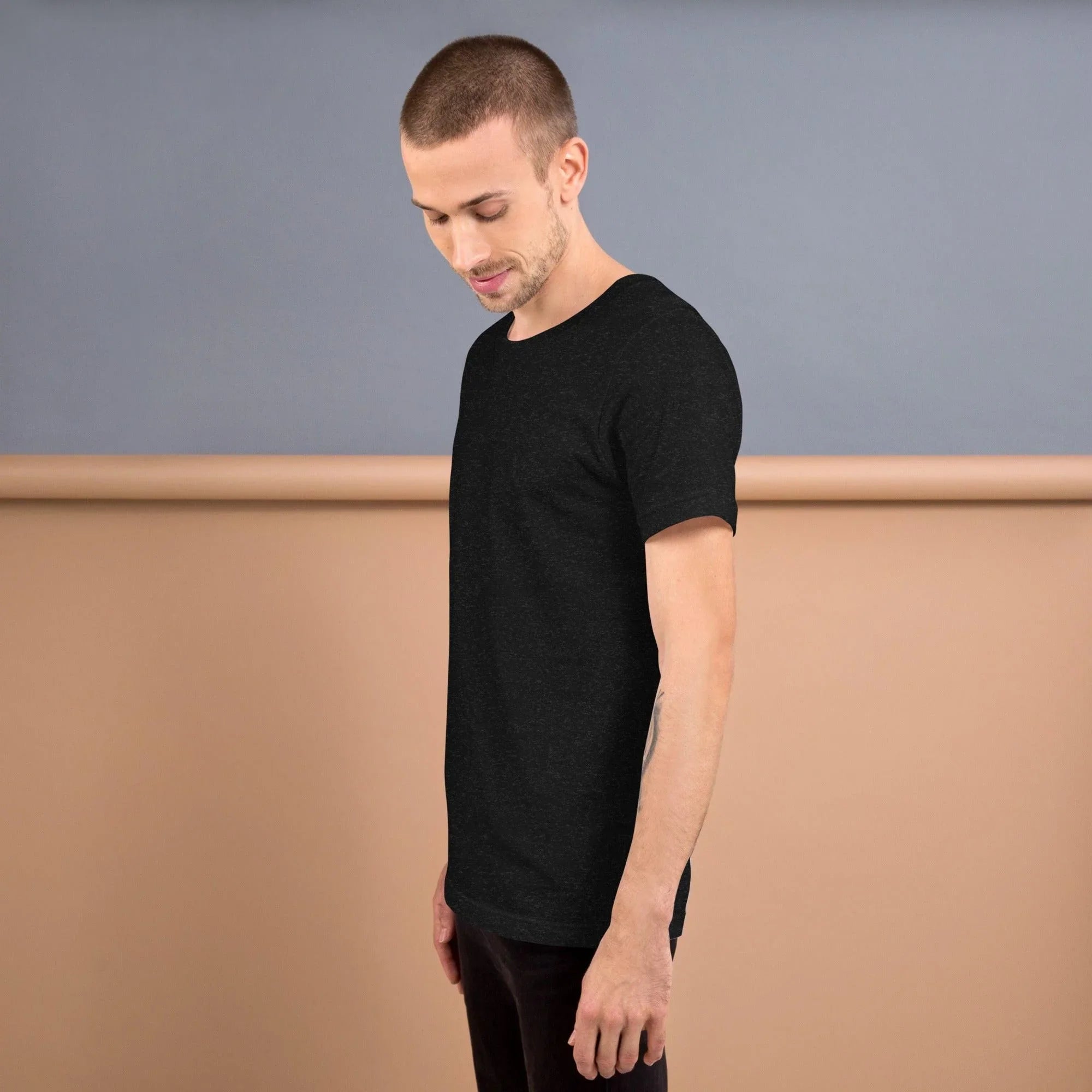 Side view of male model wearing black heather unisex staple t-shirt against beige and gray backdrop