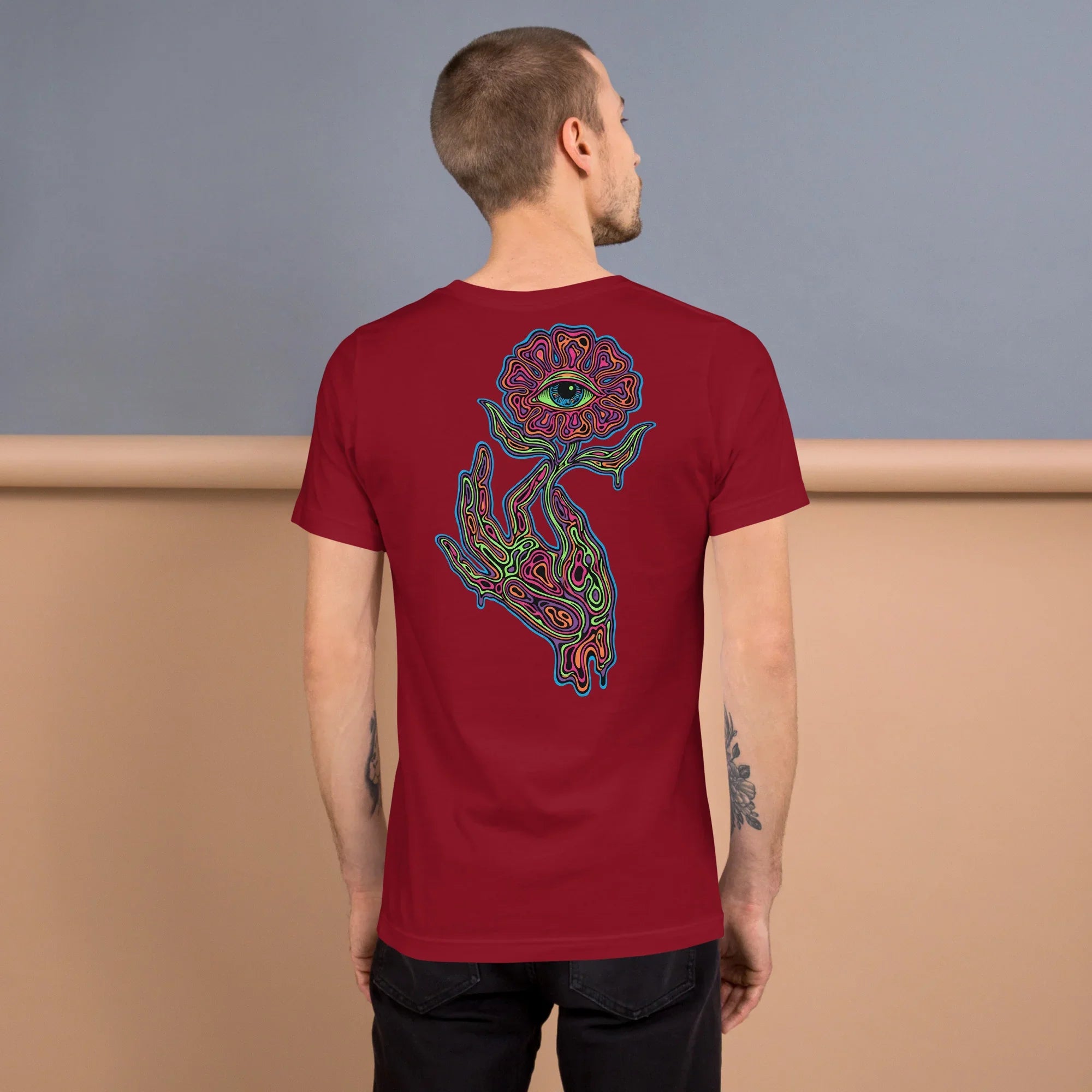 Back view of man wearing cardinal red unisex T-shirt with vibrant psychedelic hand holding eye flower design