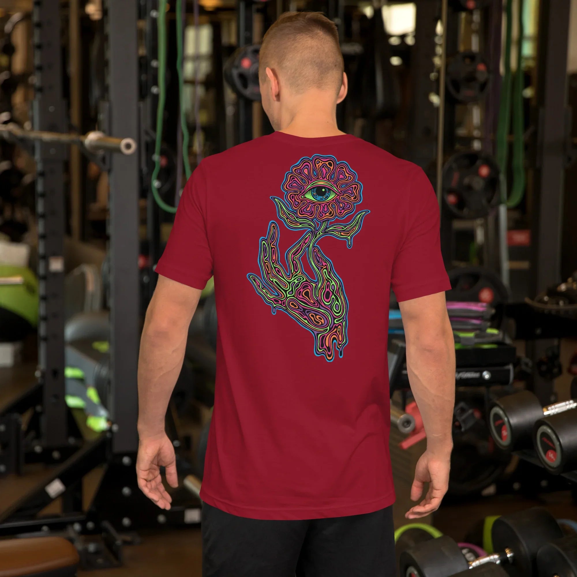 Man wearing cardinal red unisex t-shirt with psychedelic hand and eye flower design in a gym setting
