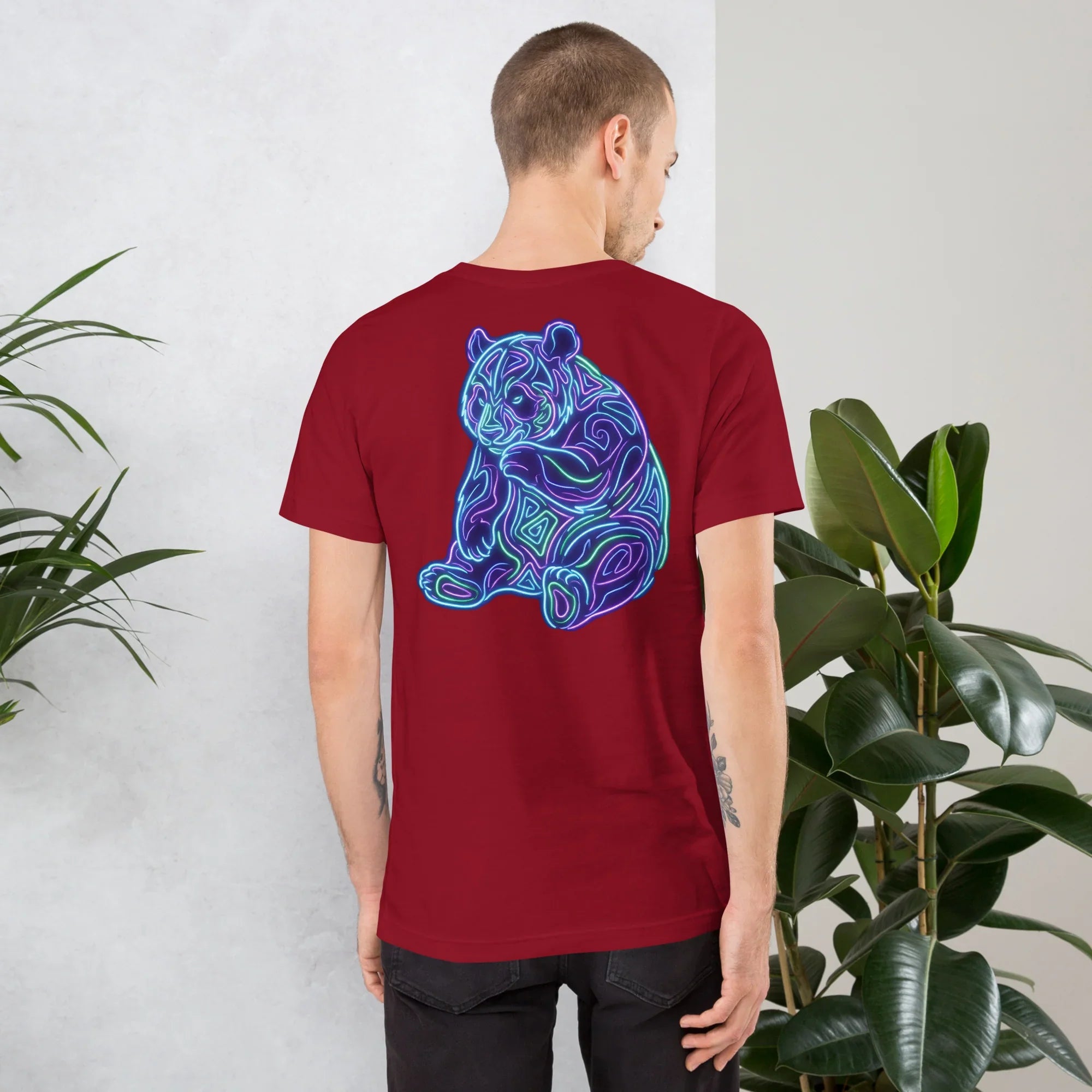 Man wearing cardinal red unisex t-shirt with neon blue and purple psychedelic bear design on back in modern indoor setting