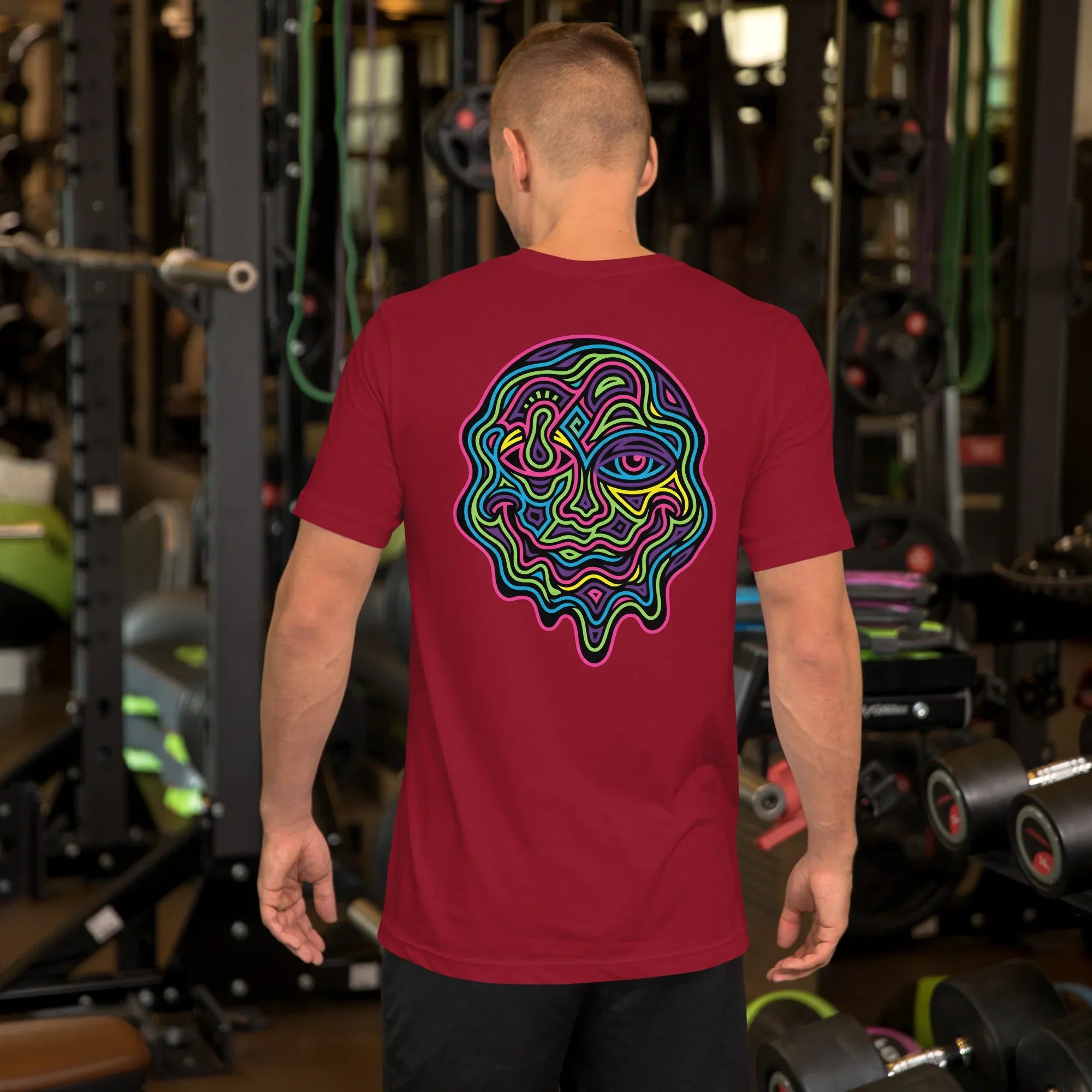 Man wearing cardinal red t-shirt with vibrant psychedelic neon abstract face design, gym background