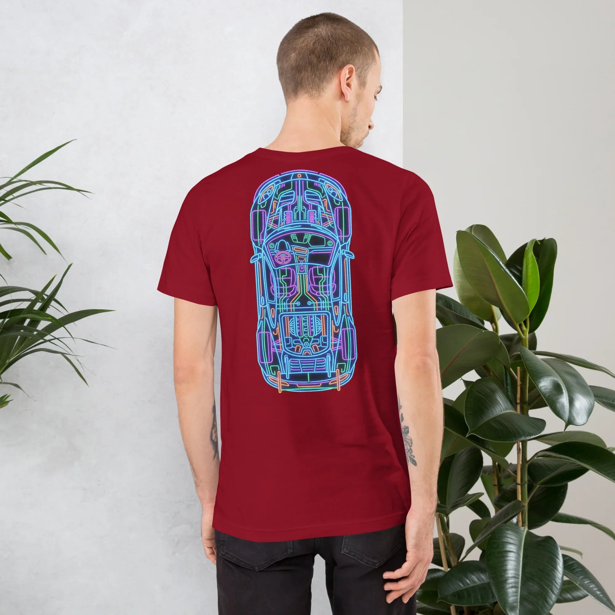 Man wearing cardinal red t-shirt with neon blue and pink car schematic design on back in indoor setting