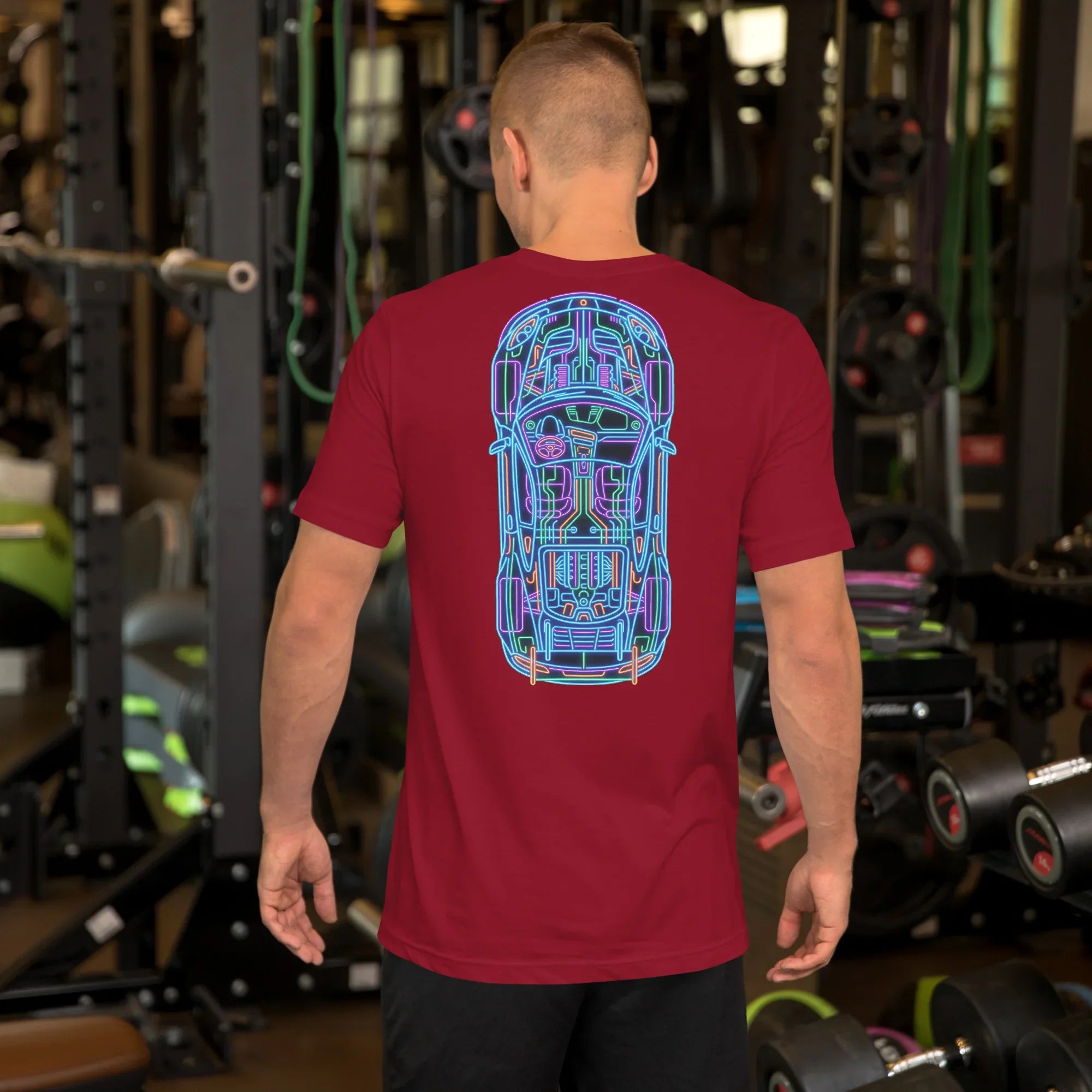 Man wearing cardinal red t-shirt with colorful neon car blueprint design on back in gym setting