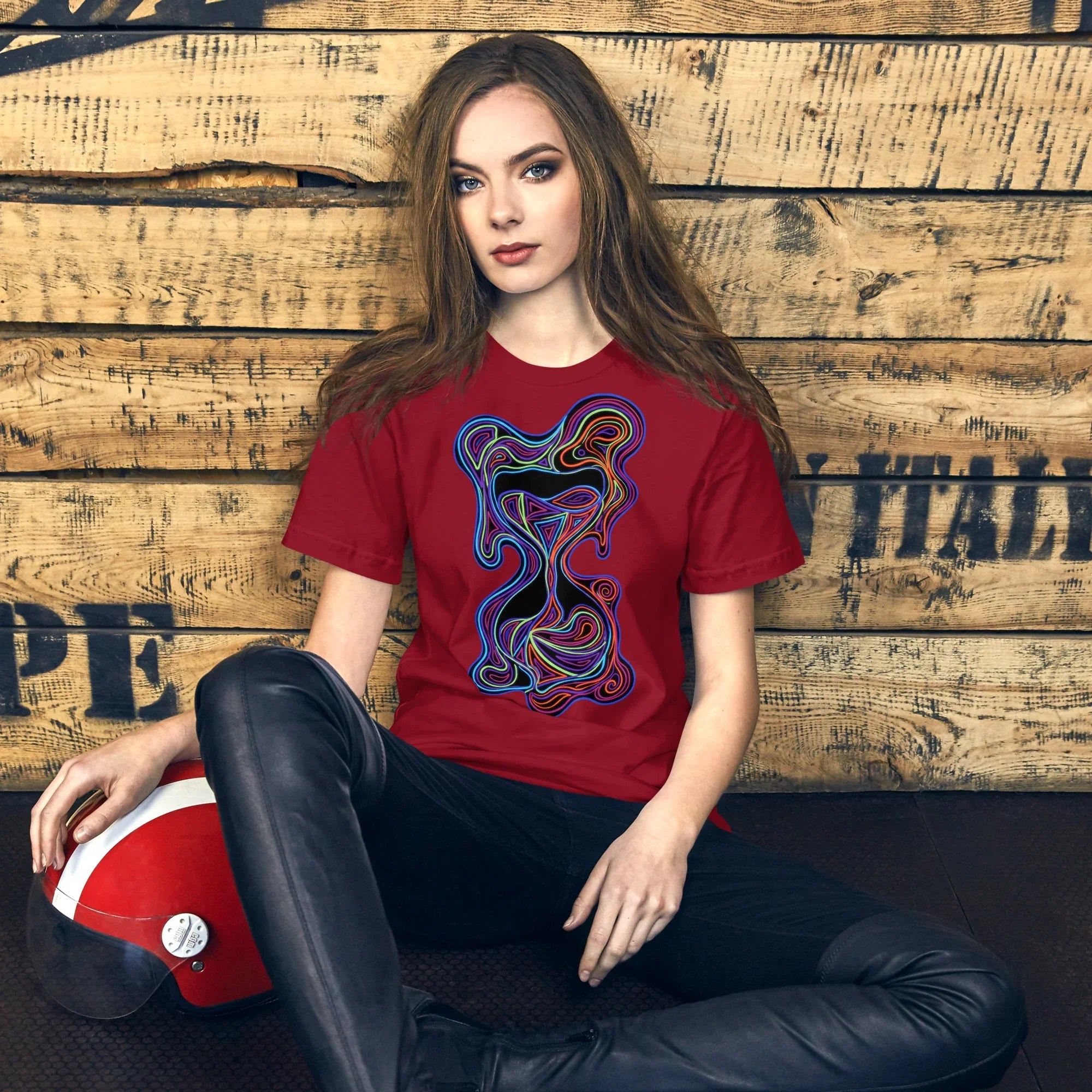 Young woman wearing cardinal red psychedelic graphic T-shirt, seated against rustic wooden wall with red vintage helmet