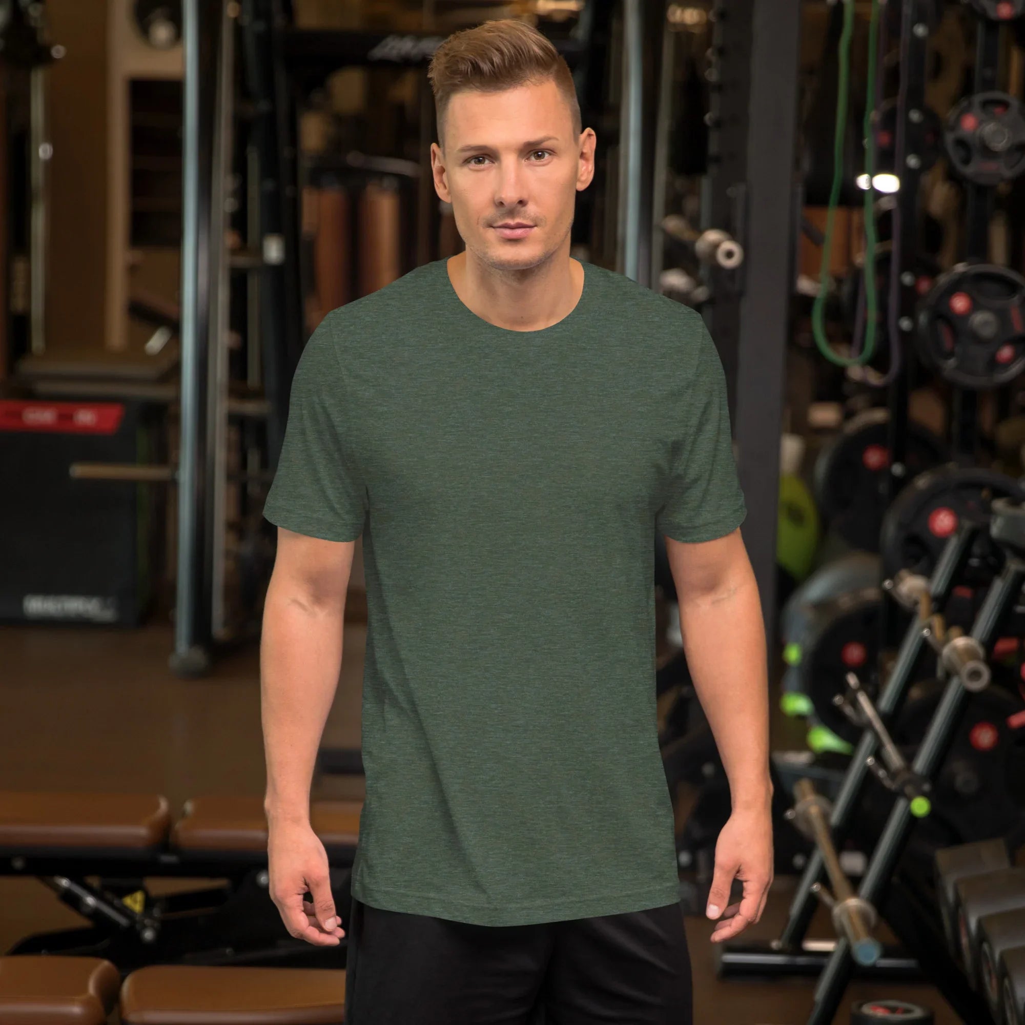 Man wearing heather forest green unisex staple t-shirt in a gym with weightlifting equipment