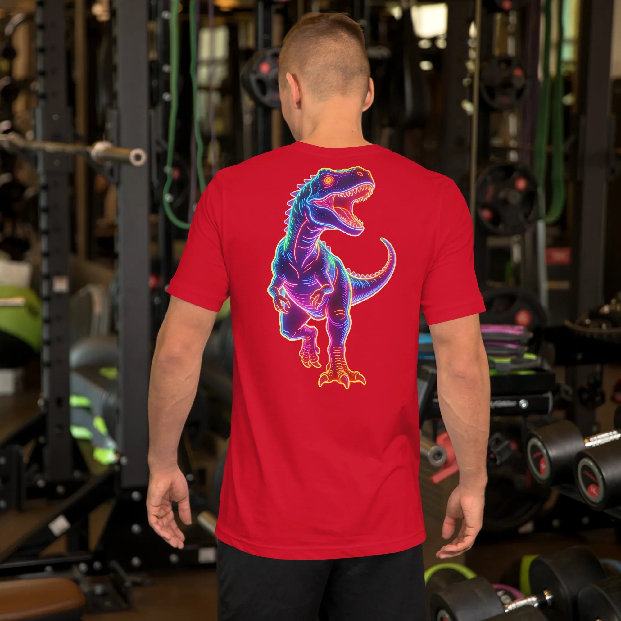 Man wearing red t-shirt with neon dinosaur graphic standing in gym with fitness equipment