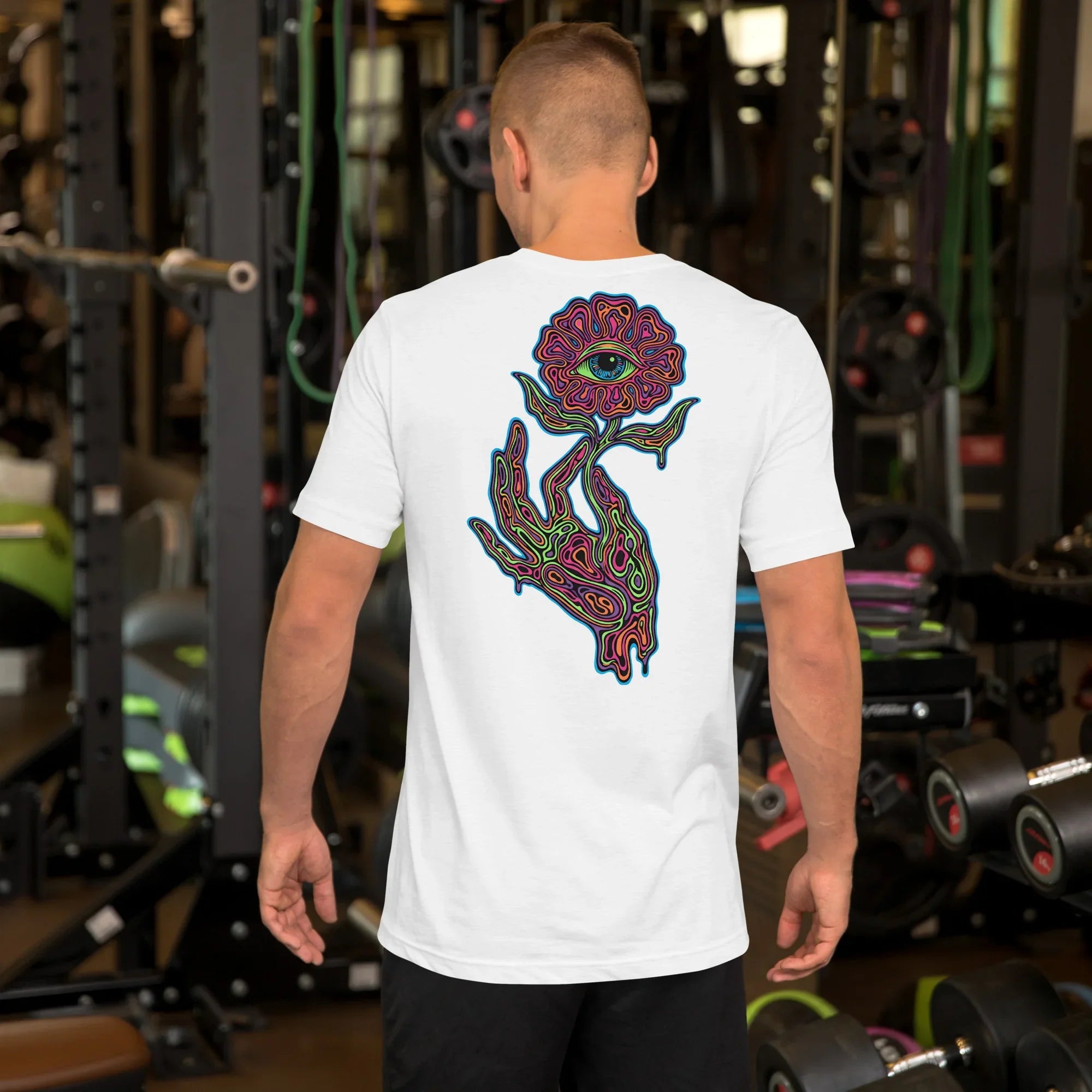 Man wearing white unisex t-shirt with psychedelic hand and eye flower graphic, gym background