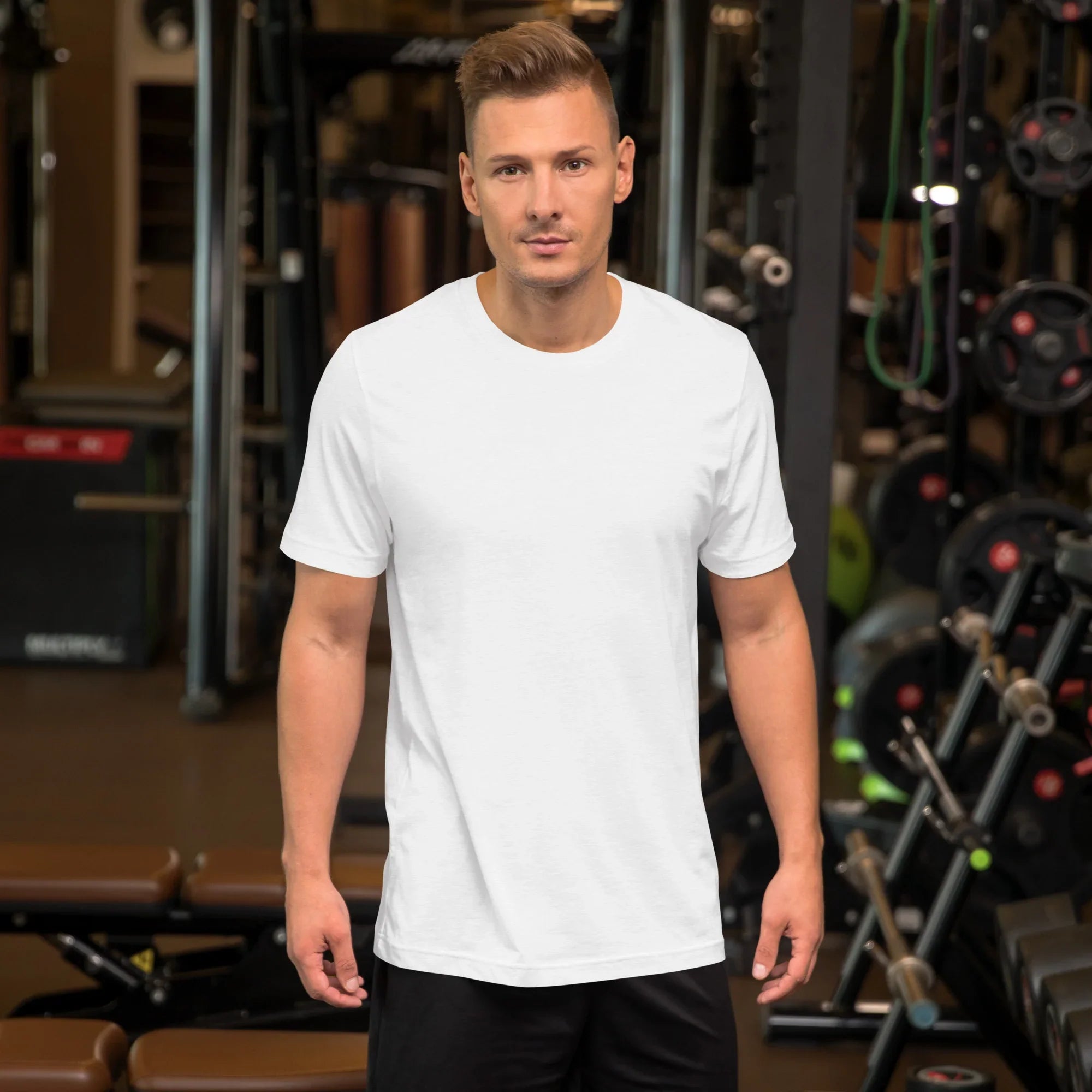 Man wearing a plain white unisex staple t-shirt in gym setting with workout equipment
